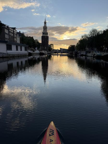 This stunning photo captures a serene evening paddle on a canal in Korte Koningsstraat, Nieuwmarktbuurt, Amsterdam, with the iconic Montelbaanstoren reflected perfectly in the calm water